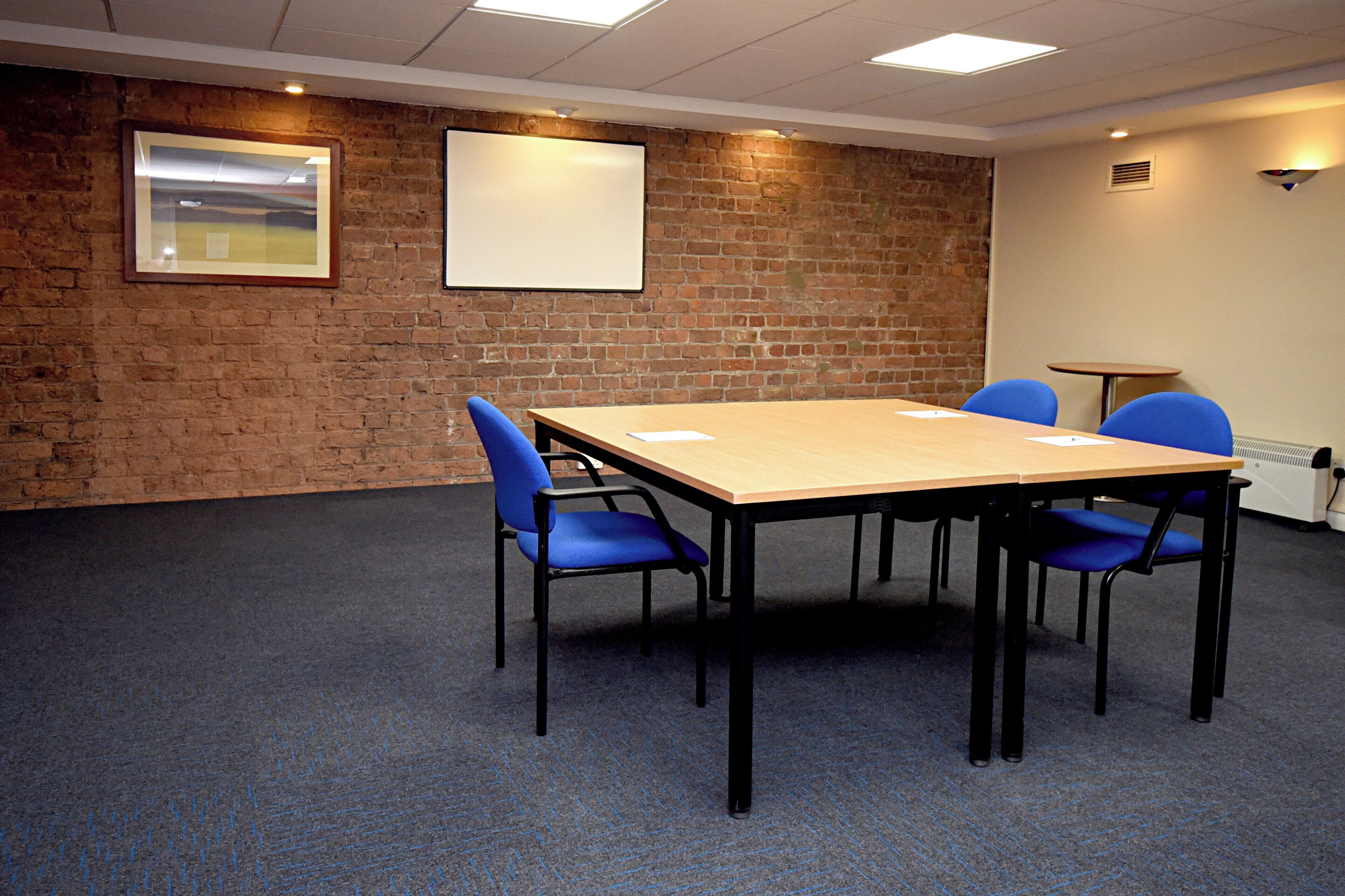 A conference room with a brick wall, a wooden table, and blue chairs.