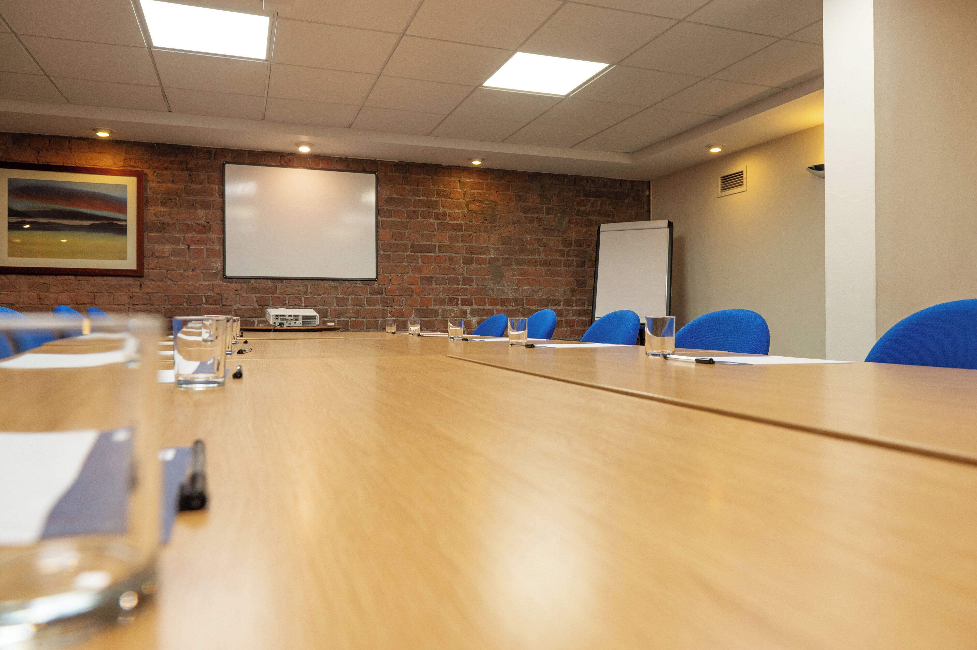 Una sala de conferències amb una taula llarga, cadires blaves, una pissarra i un projector.