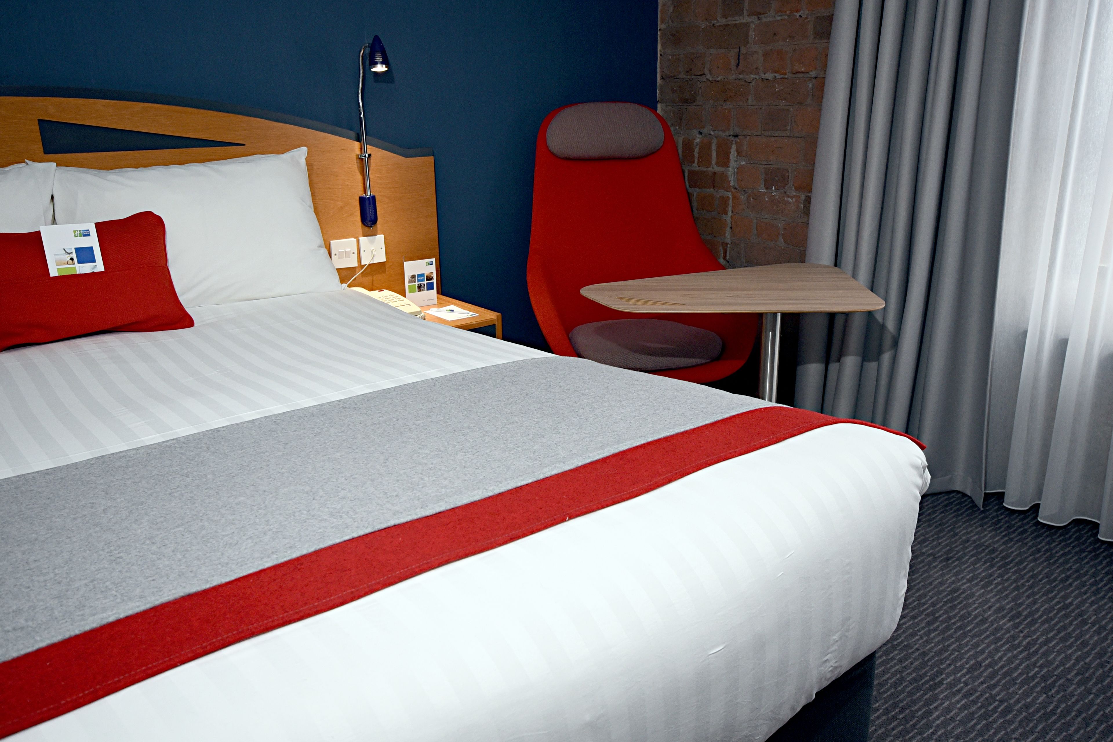 A hotel room with a large bed, a red chair, a small table, and a nightstand.