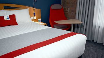 A hotel room with a large bed, a red chair, a small table, and a nightstand.