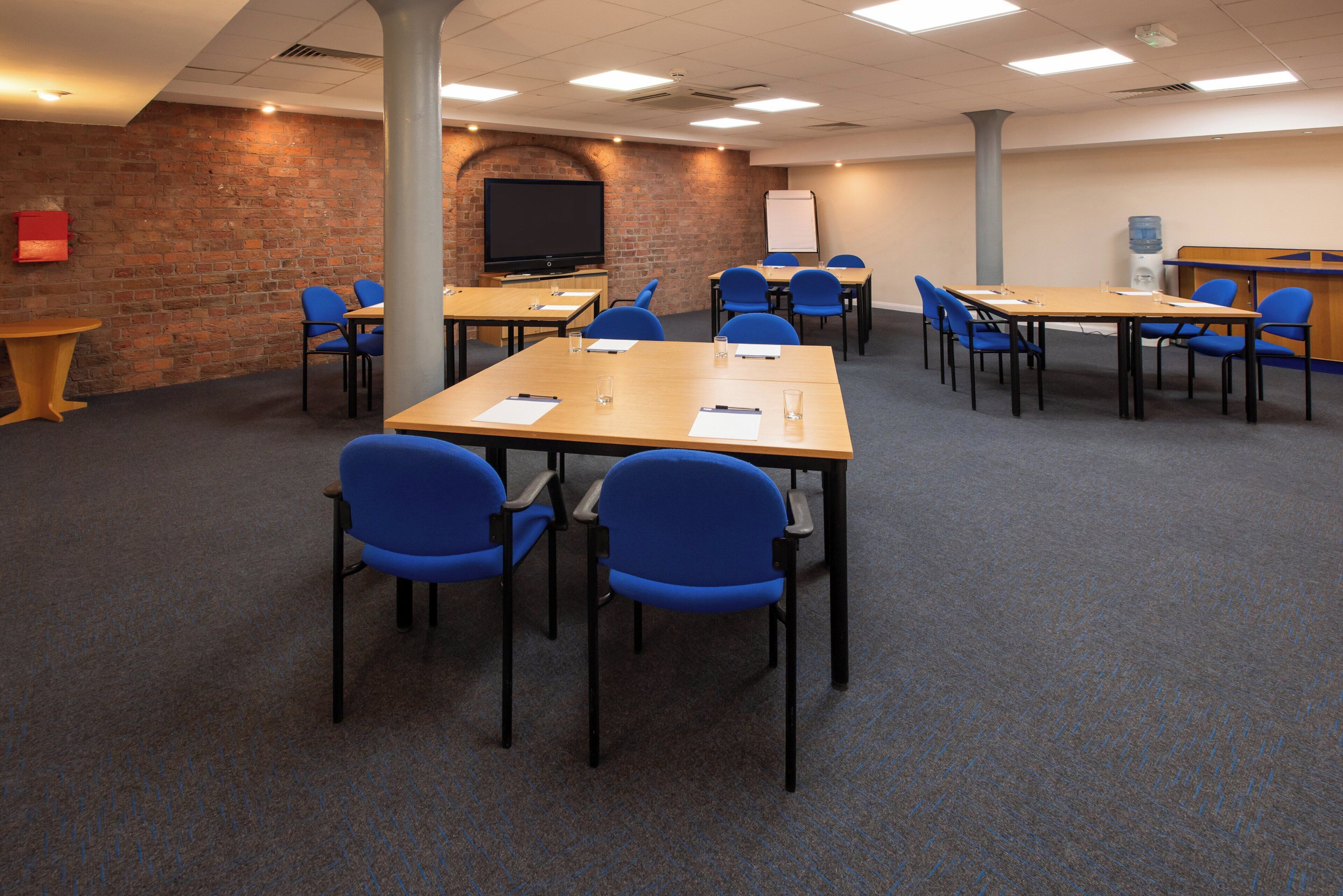 A conference room with tables and chairs, a brick wall, and a whiteboard.