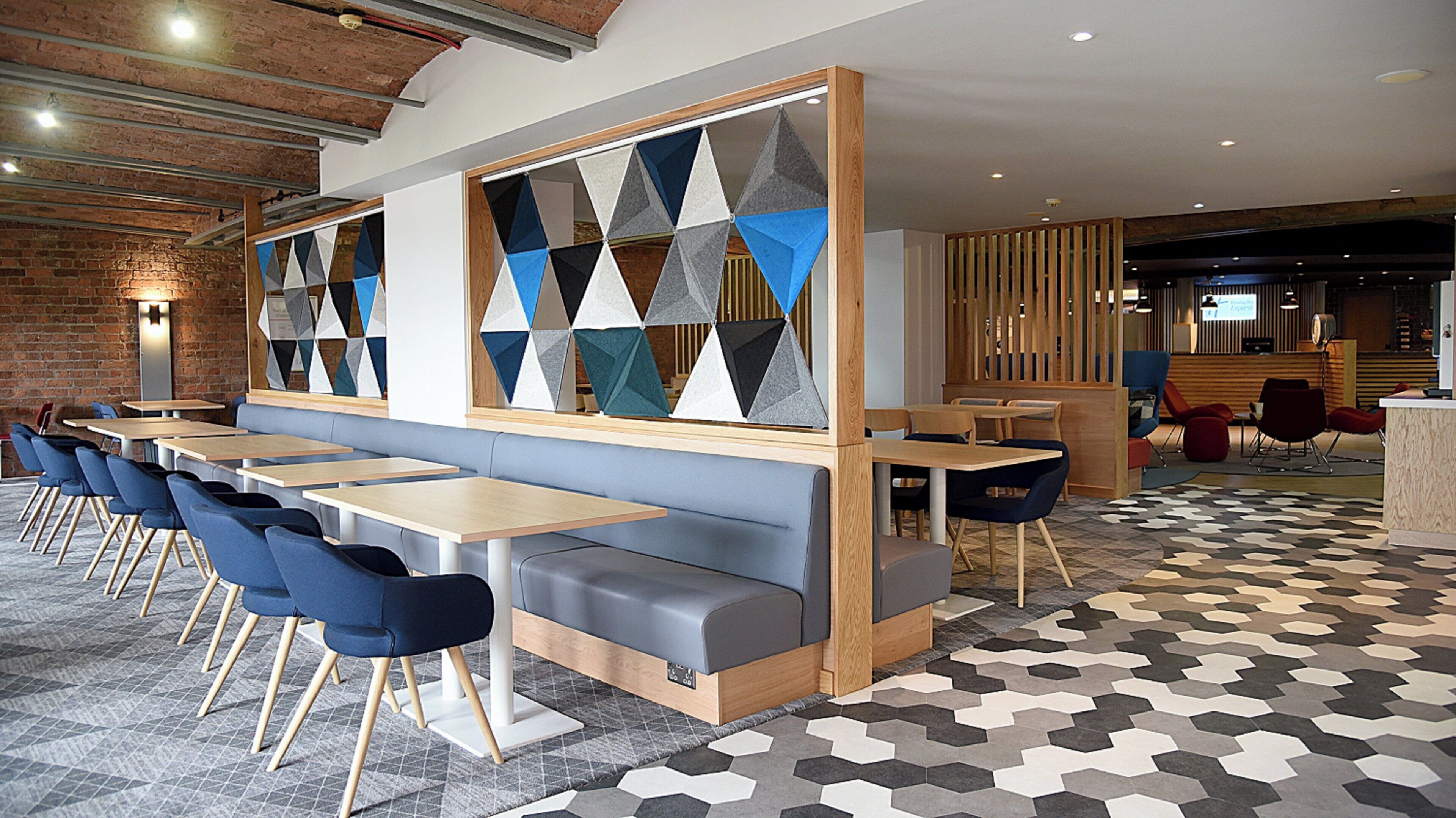 Un restaurante moderno con una barra larga, sillas azules y una pared con estampado geométrico.