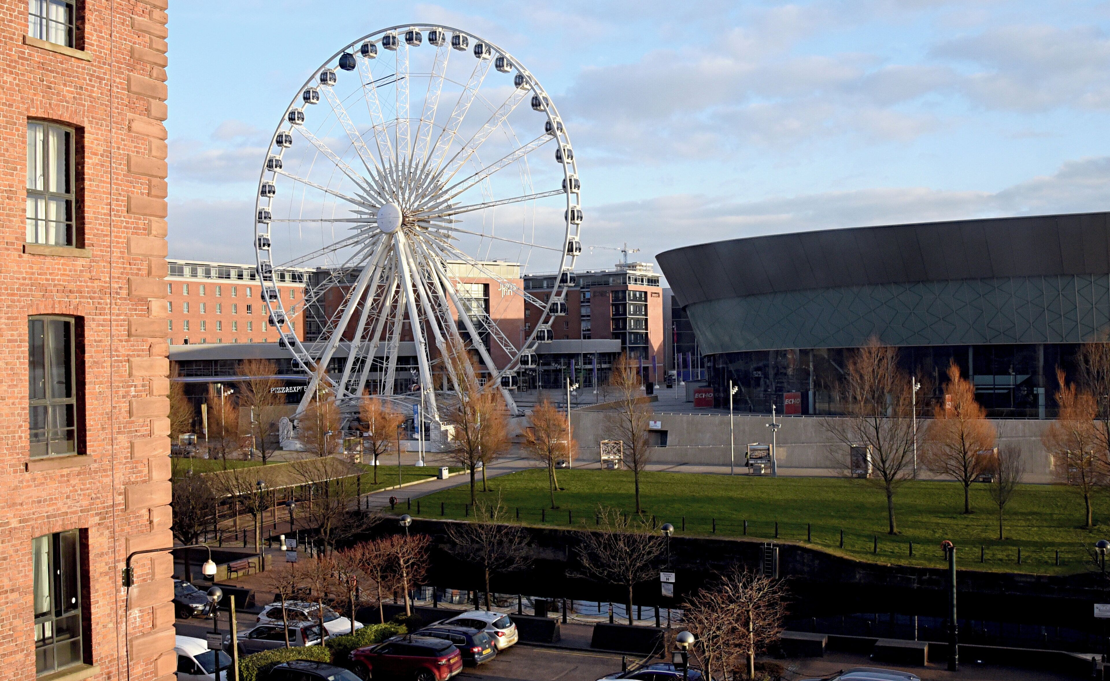 Ein Riesenrad, ein modernes Gebäude und ein Parkplatz mit Autos.