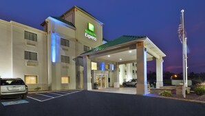 A Holiday Inn Express building with a well-lit entrance, a parking area, and an American flag.