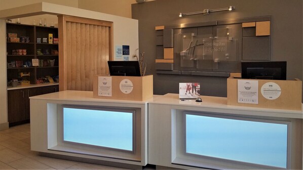 A reception desk with a digital display, a check-in counter, and a shelf with snacks. - Holiday Inn Express Irwin (Pa Tpk Exit 67) by IHG (Irwin)