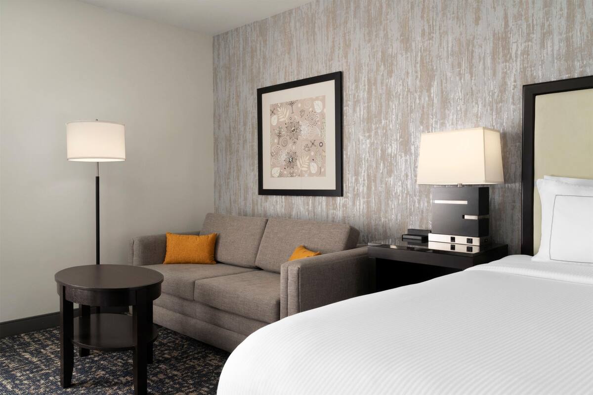 A hotel room with a bed, a sofa, a small table, a lamp, and a framed picture on the wall.