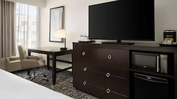 Habitación de hotel con cama, escritorio con silla, cómoda con televisor, microondas y refrigerador.