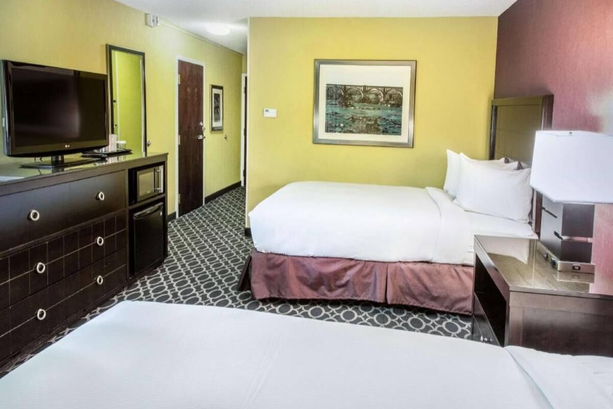 A hotel room with a bed, a TV, a dresser, and a painting on the wall.