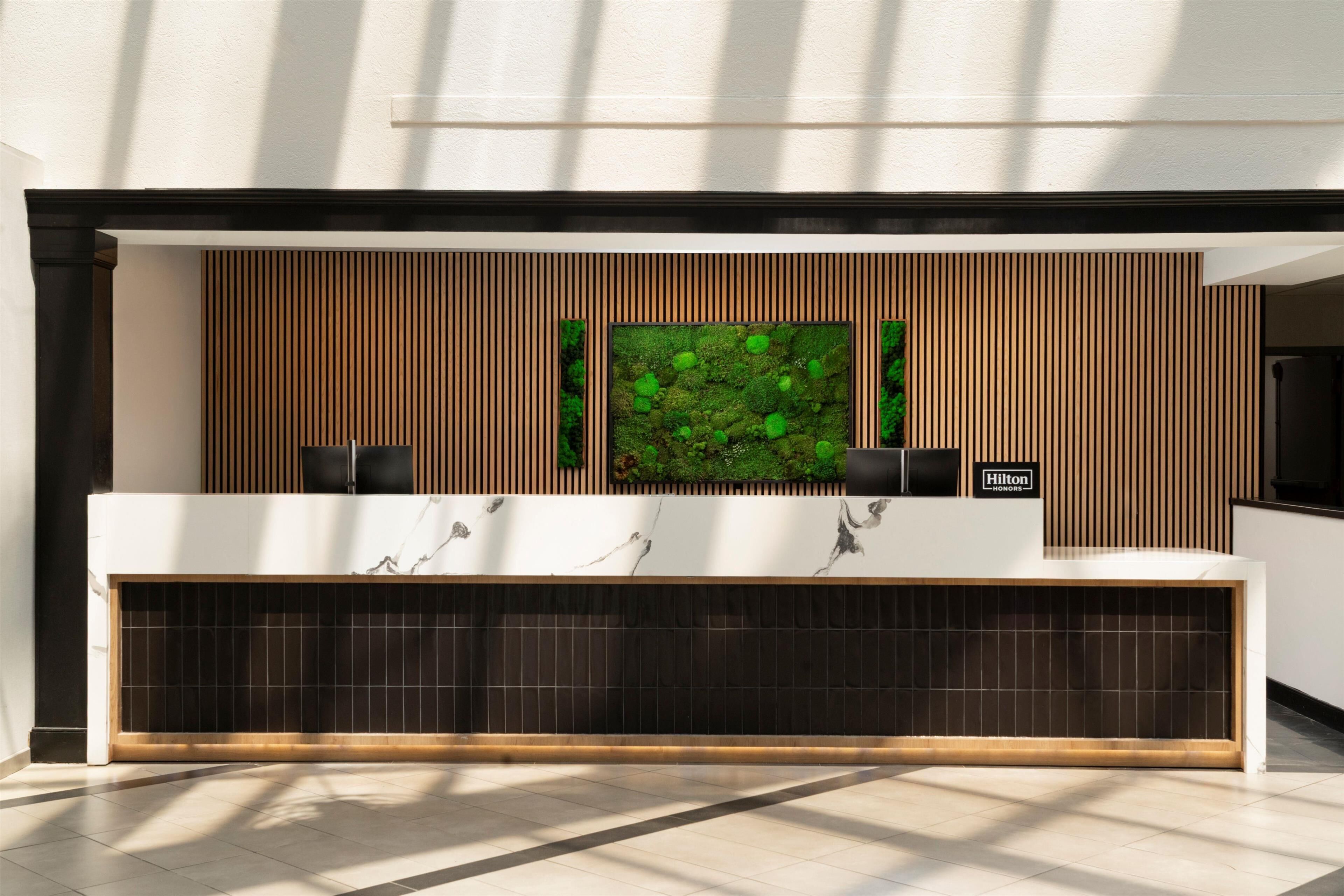 A modern reception desk with a wooden panel wall, a green moss wall art piece, and a sign that reads "Hilton".