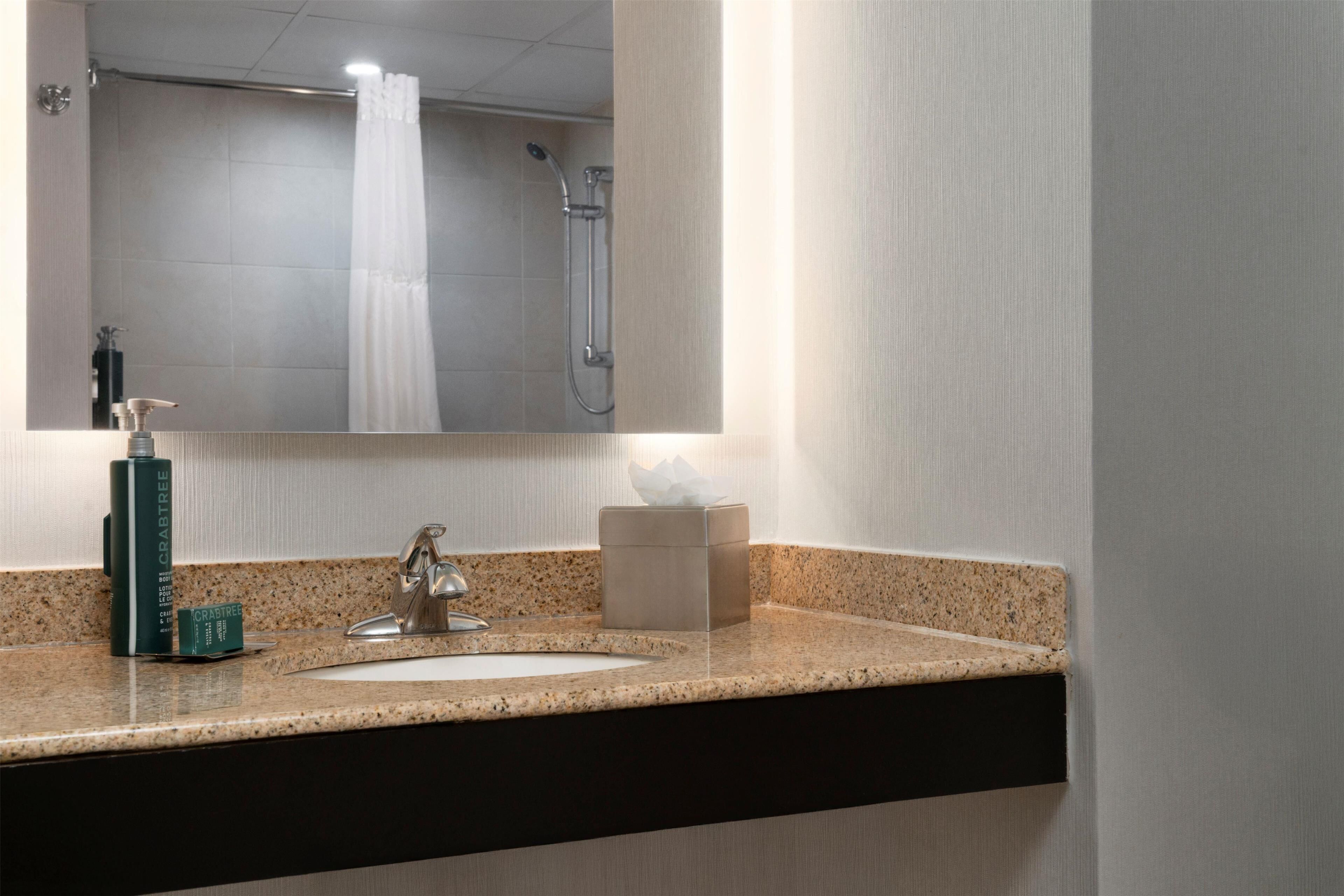 Baño con encimera de granito, lavamanos, espejo y ducha.