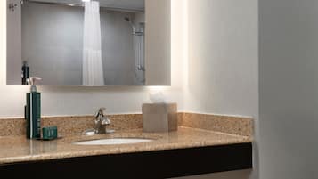 Baño con encimera de granito, lavamanos, espejo y ducha.