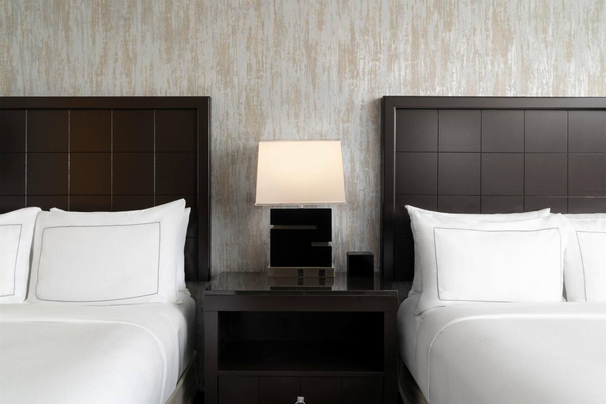 A hotel room with two beds, a nightstand with a lamp, and a wall with a textured pattern.