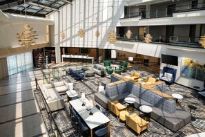 Eine geräumige Lobby mit mehreren Sitzbereichen, einem Empfangstresen und einer Treppe zu einer oberen Ebene.