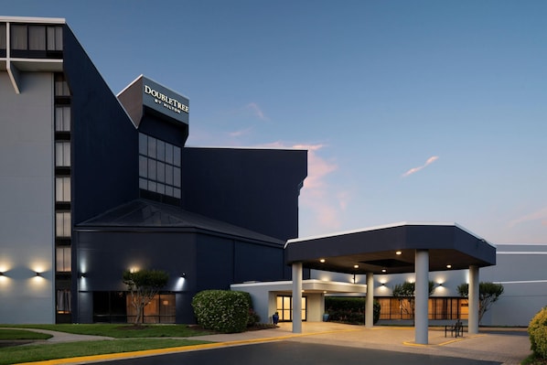 Un hotel moderno con fachada oscura, un área de entrada techada y un letrero que indica que es un DoubleTree by Hilton.