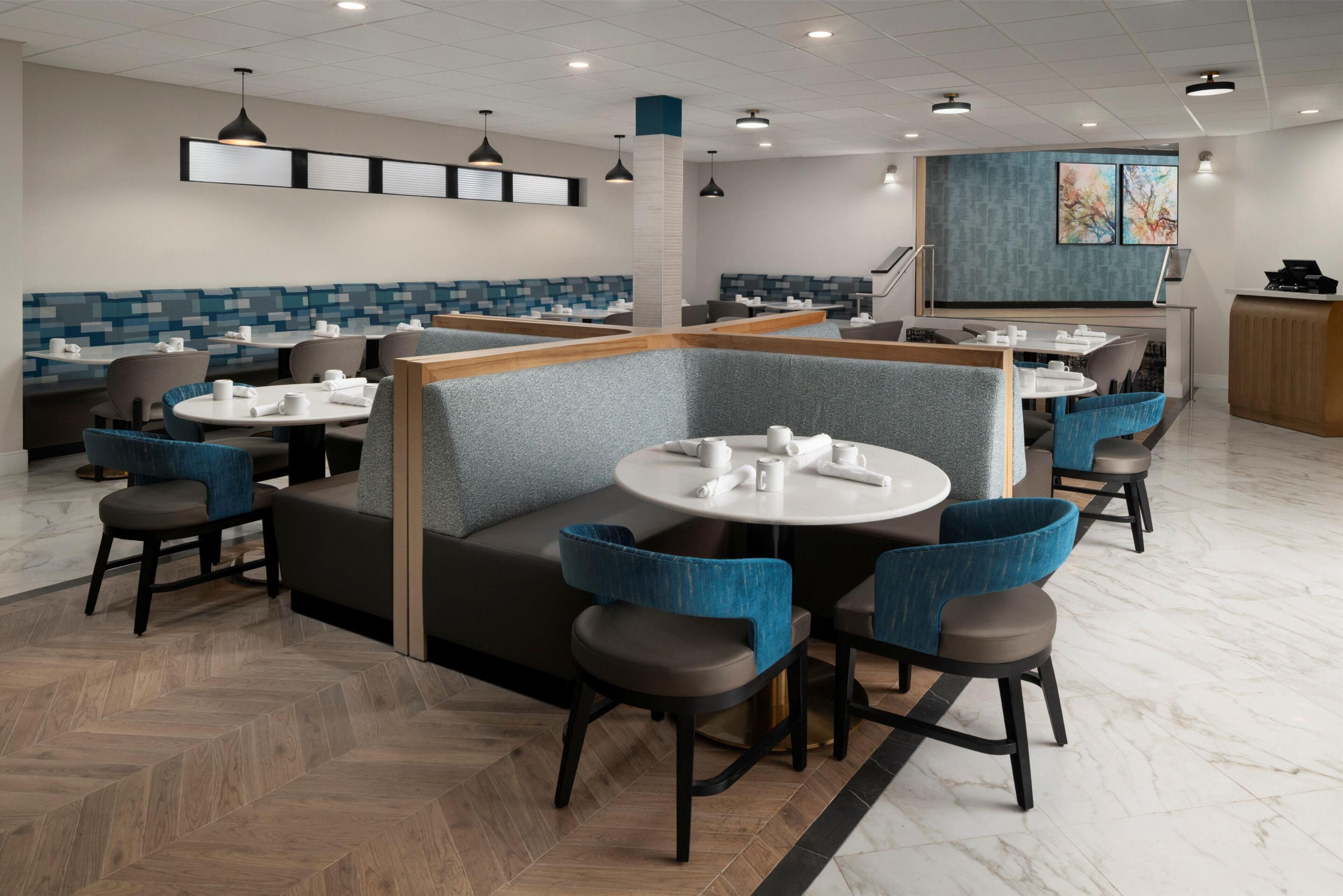 Ein modernes Restaurant mit Boxsitzgelegenheiten, runden Tischen und blau gepolsterten Stühlen.