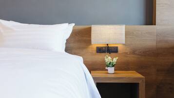 Ein ordentlich bezogenes Bett mit weißen Bettwäsche, ein Nachttisch aus Holz mit einer Lampe und einem kleinen Topfpflanzen, sowie ein an der Wand befestigtes Telefon.