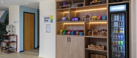 Quarto com um armário de madeira contendo lanches, uma máquina de venda automática de bebidas e uma placa para a Garnier Shop.