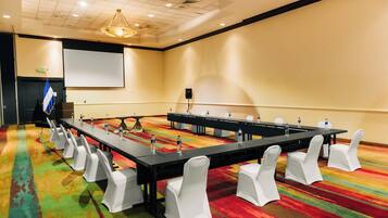 A conference room with a long table, white chairs, and a projector screen.