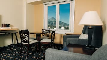 A hotel room with a dining area, a sofa, a lamp, and a window with a mountain view.