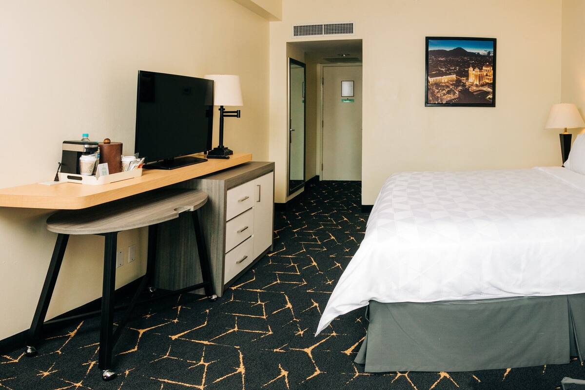 Una habitación de hotel con una cama, un escritorio con televisor, una lámpara y un teléfono en la mesita de noche.
