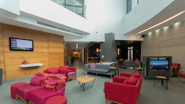 Un hall d’entrée moderne avec des sièges rouges et gris, un téléviseur à écran plat et un mur décoratif en bois.