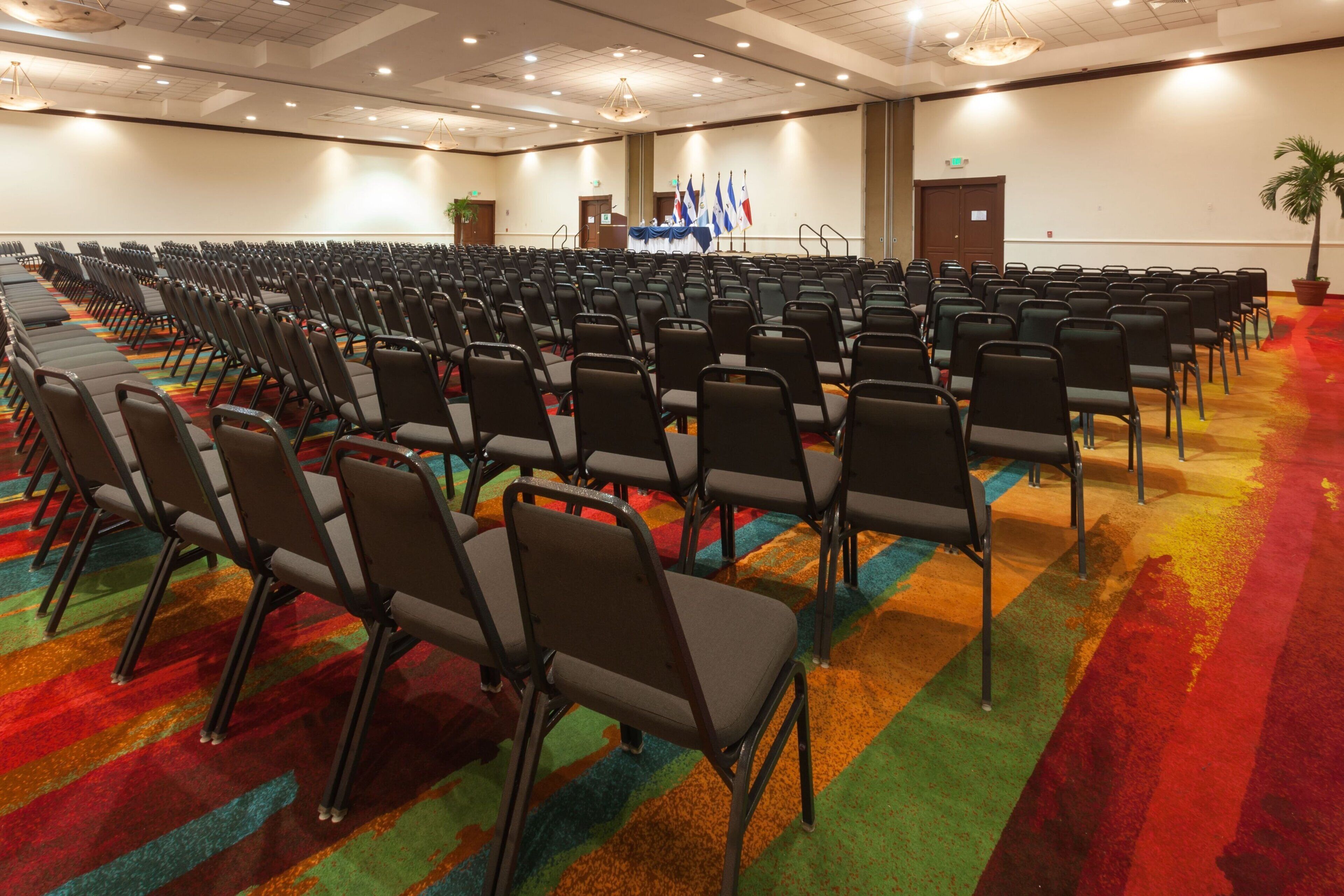 Un salón de conferencias con filas de sillas y un escenario con banderas.