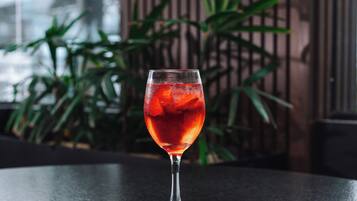Un bicchiere di vetro trasparente con cubetti di ghiaccio e una bevanda rossa su un tavolo scuro.
