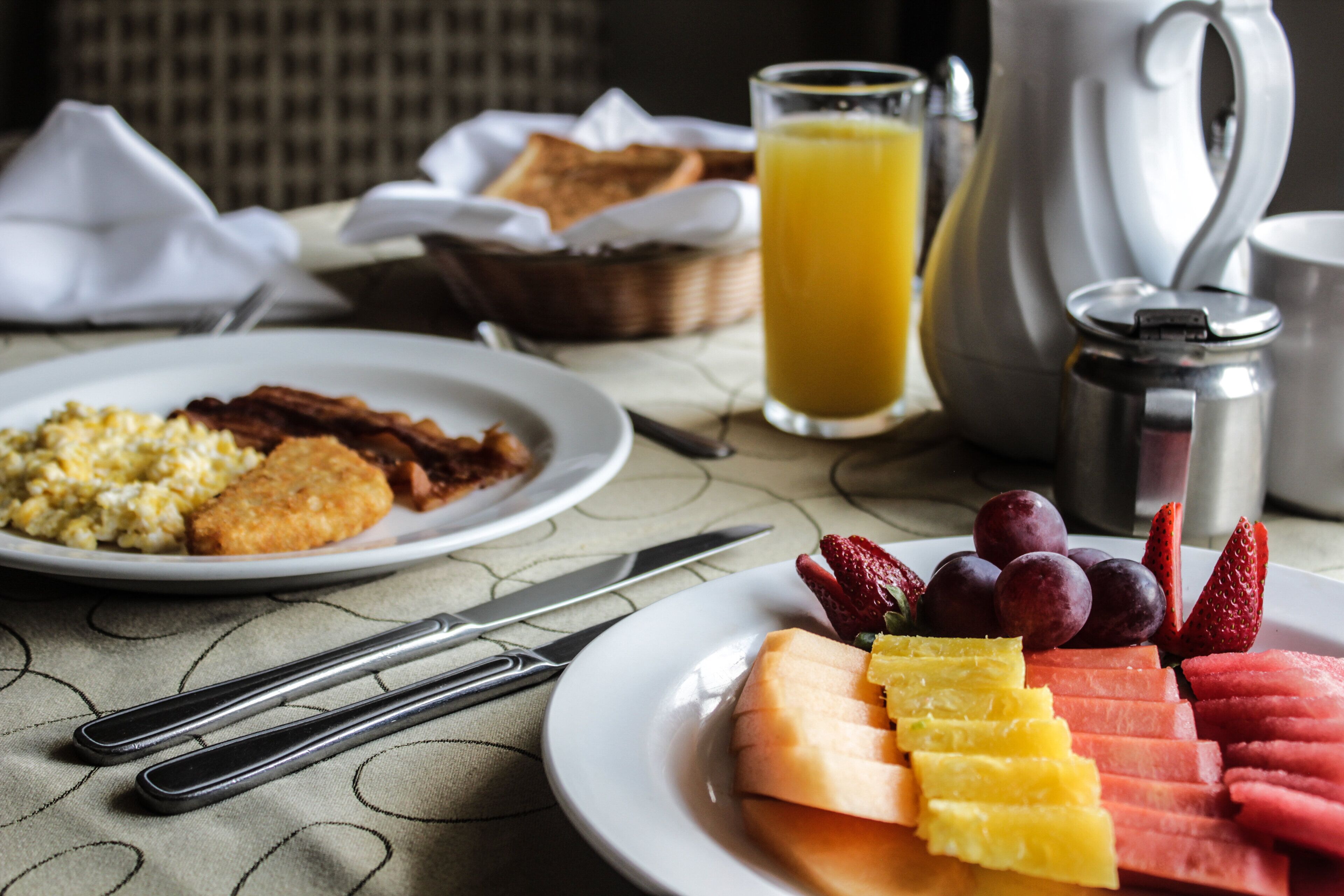 Un desayuno con platos de comida, un vaso de zumo de naranja y una cafetera.