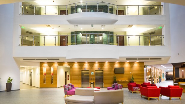 Un hall d’hôtel à plusieurs niveaux, doté d’un espace salon central, d’ascenseurs et d’un comptoir d’accueil.