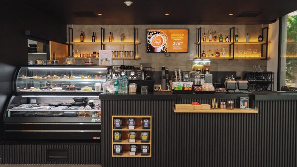 A modern cafe with a display case of pastries, a coffee bar, and shelves of beverages. - Holiday Inn San Salvador by IHG (Antiguo Cuscatlán)