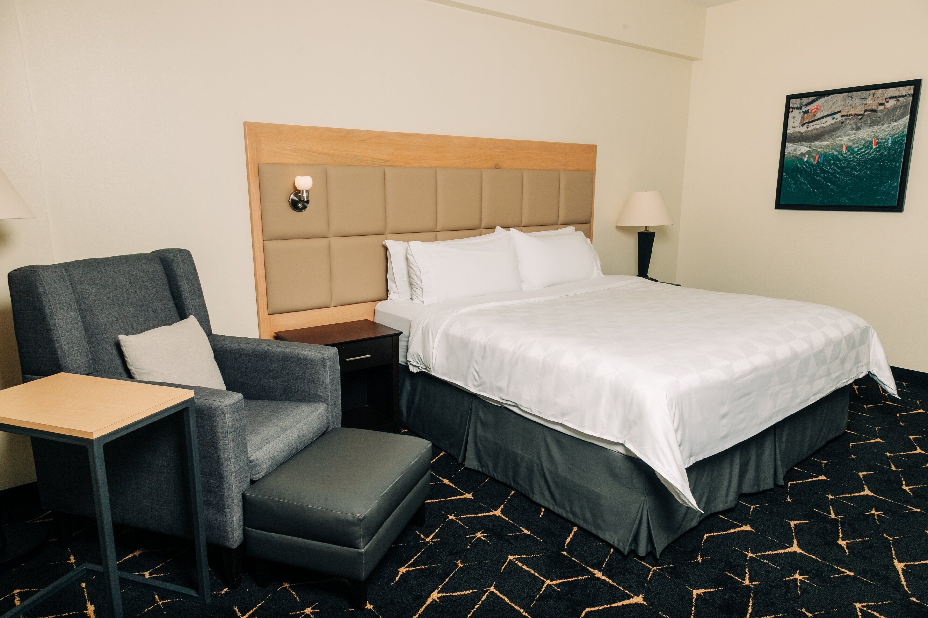 A hotel room with a bed, a chair, a nightstand, and a lamp.
