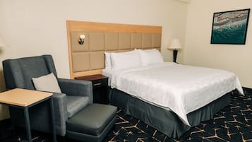 A hotel room with a bed, a chair, a nightstand, and a lamp.