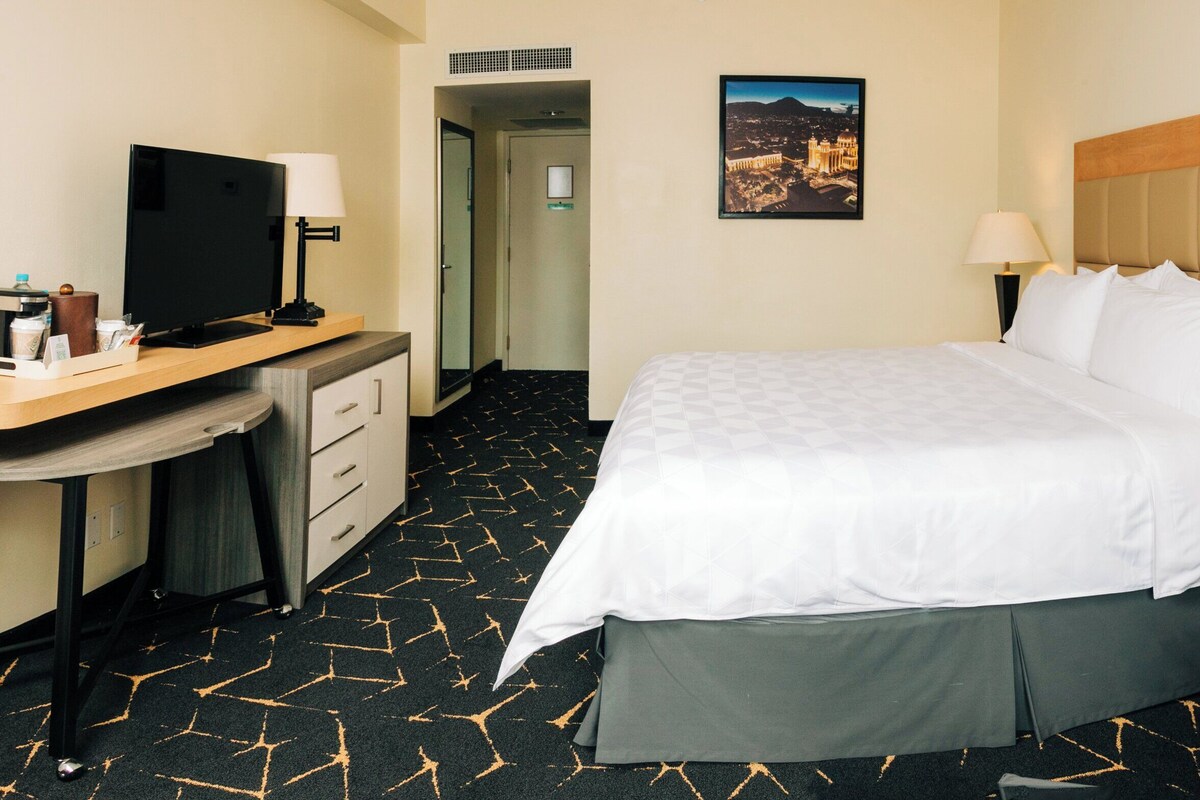 Una habitación de hotel con una cama, un escritorio con televisor, una lámpara y un teléfono en la mesita de noche.