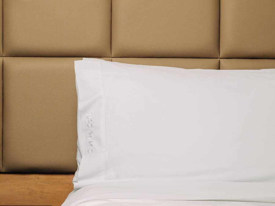 A bed with a beige upholstered headboard and a white pillow with the text "Suave/Soft" on it.