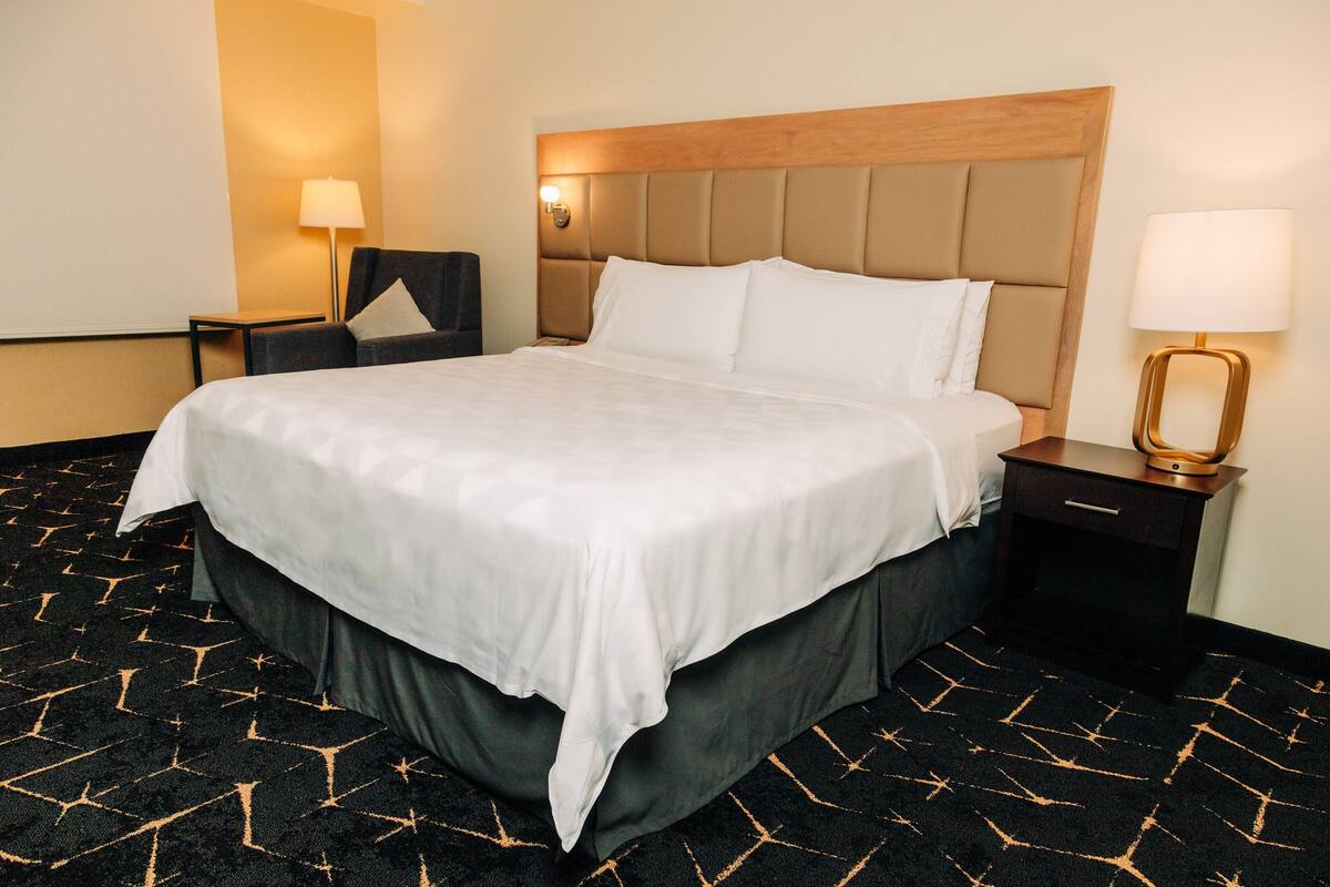Una habitación de hotel con una cama grande, una mesita de noche, una silla y una lámpara.