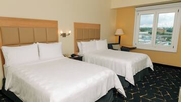 A hotel room with two beds, a window with a city view, and a patterned carpet.