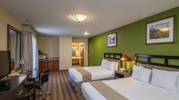 Habitación de hotel con dos camas, un escritorio, una silla, un televisor y un baño visible a través de una puerta abierta.