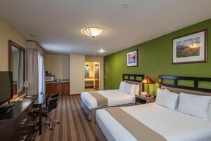 A hotel room with two beds, a desk, a chair, a TV, and a bathroom visible through an open door.