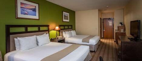 A hotel room with two beds, a desk, a chair, a television, and artwork on the walls.
