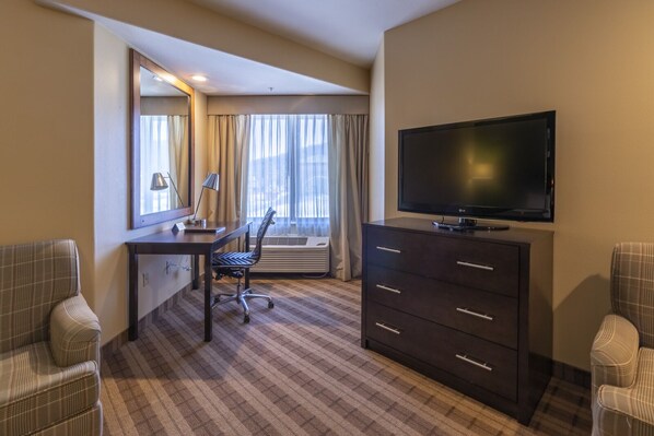 Habitación de hotel con una televisión de pantalla plana grande, un escritorio con silla, cómoda y dos sillones.