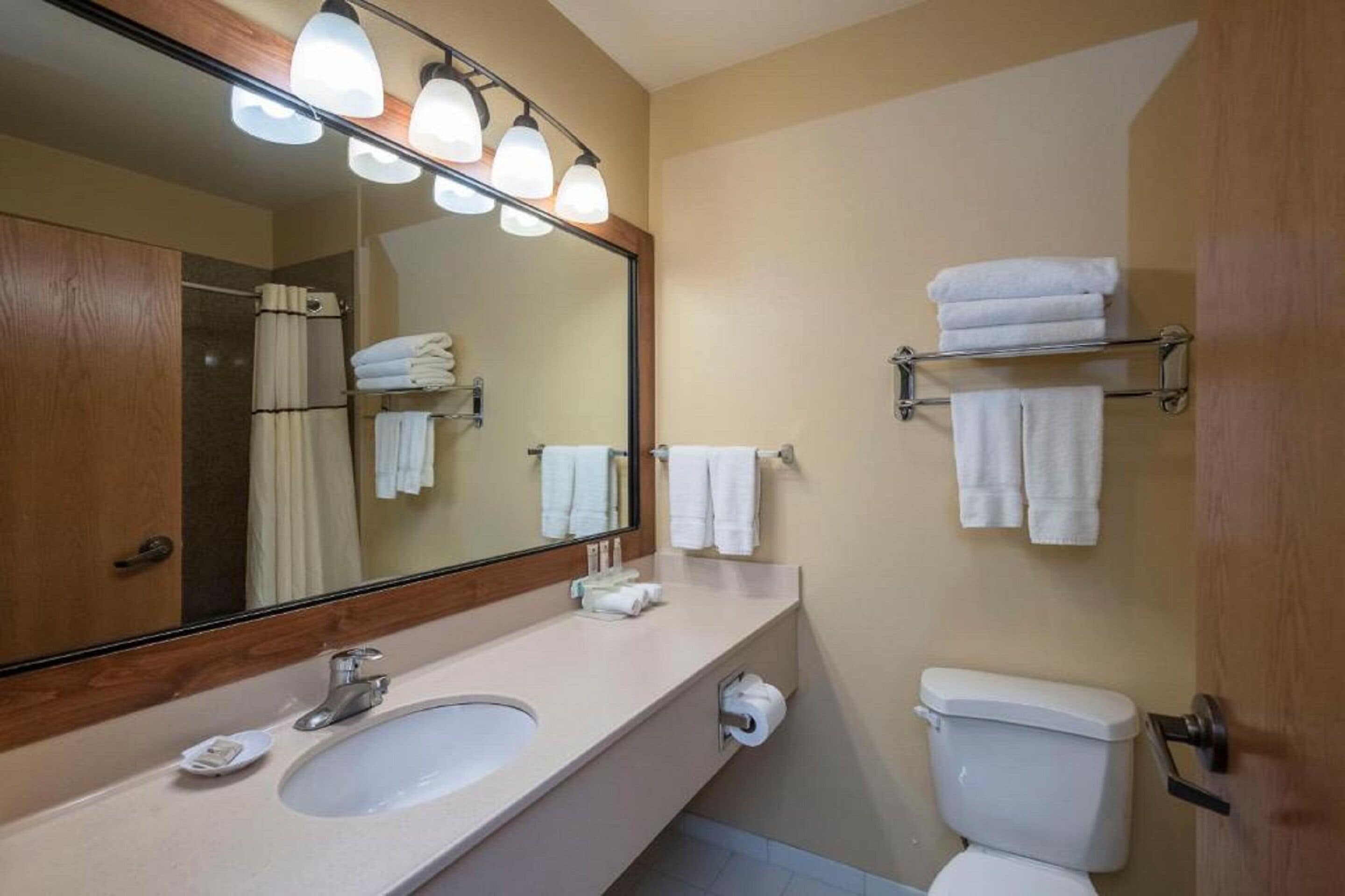 Un baño con lavamanos, espejo y retrete. Hay toallas en un estante y un perchero.