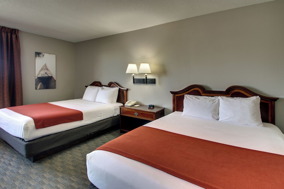 A hotel room with two beds, a nightstand with a lamp, a painting on the wall, and a telephone on the nightstand.