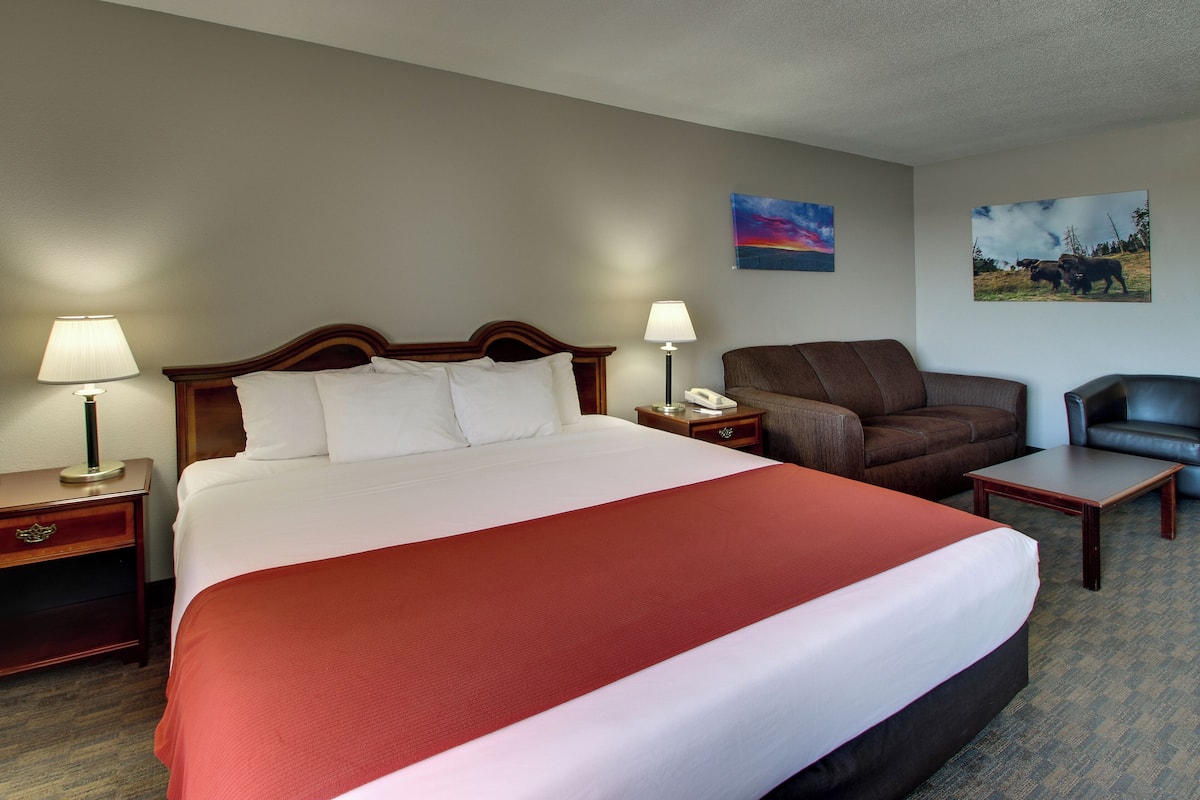 A hotel room with a large bed, two bedside tables with lamps, a brown leather armchair, a small table, and two wall-mounted lamps.