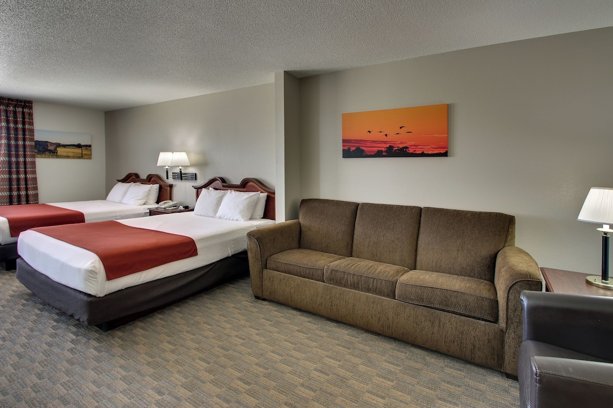 A hotel room with two beds, a sofa, a desk, and a painting of a sunset.