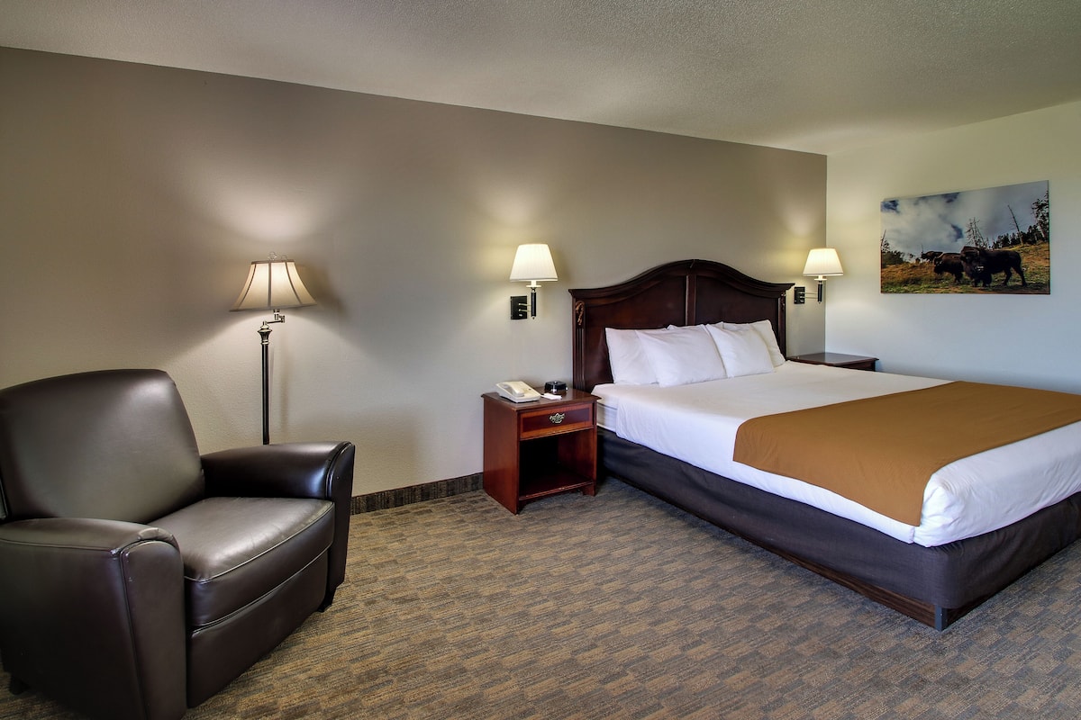 A hotel room with a large bed, a leather chair, a nightstand with a lamp, and a painting on the wall.