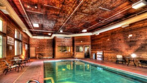 An indoor swimming pool with wooden walls and ceiling, surrounded by seating and a visible door. - The Niobrara Lodge (Valentine)