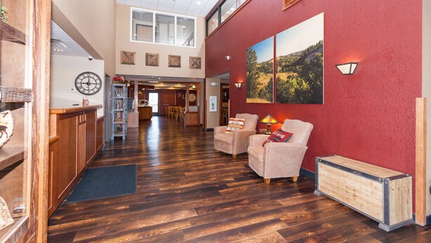 A spacious lobby with wooden flooring, a reception desk, two armchairs, and a large wall-mounted painting. - The Niobrara Lodge (Valentine)