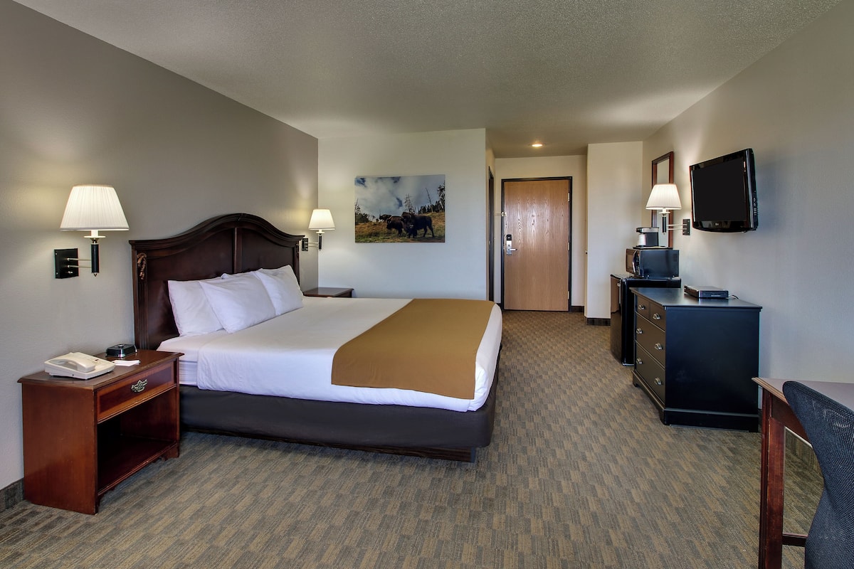A hotel room with a large bed, bedside lamps, a television, a desk, and a door leading to another room.