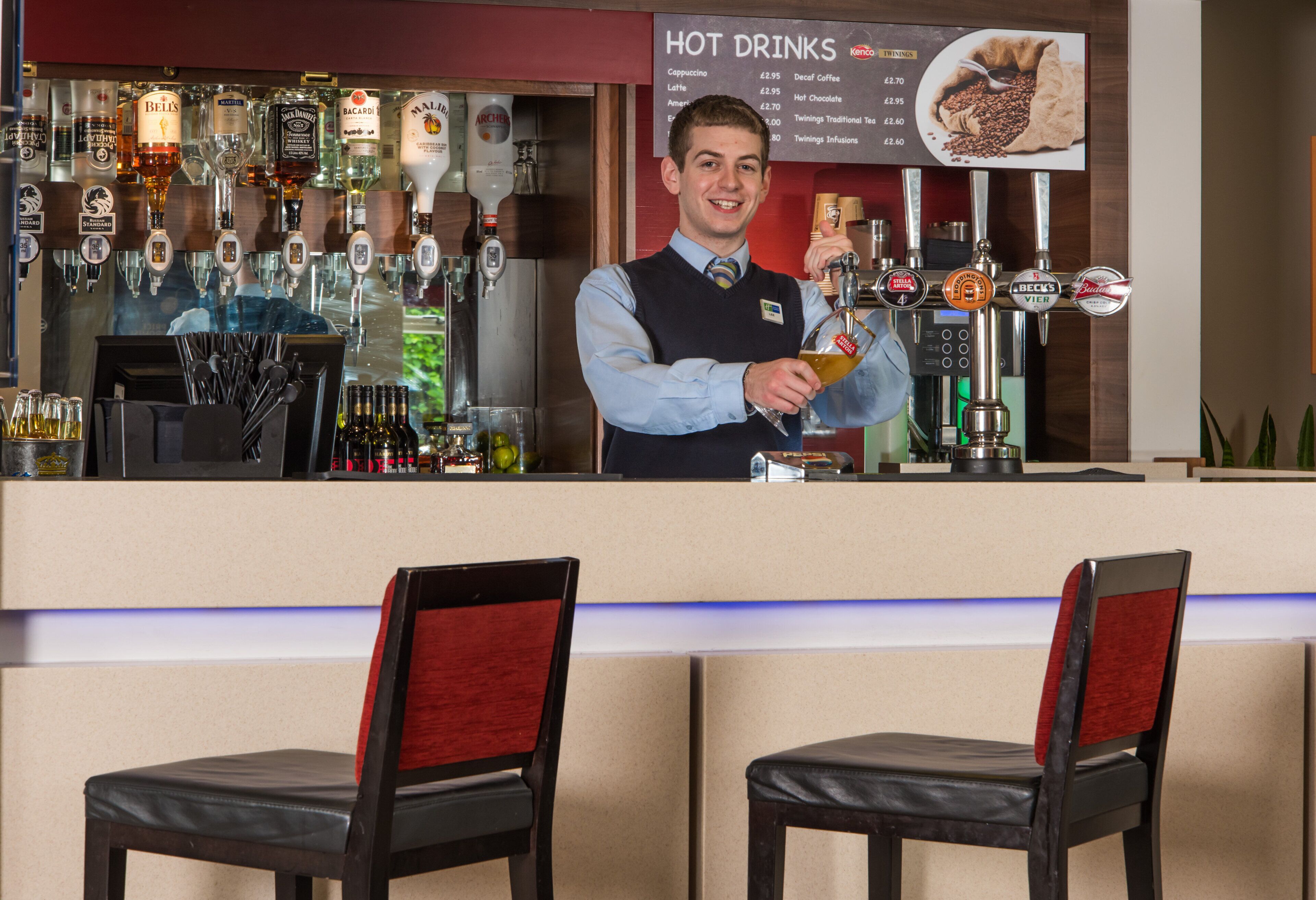 Zona de bar con varios dispensadores de bebidas, un cartel con la carta y dos sillas.