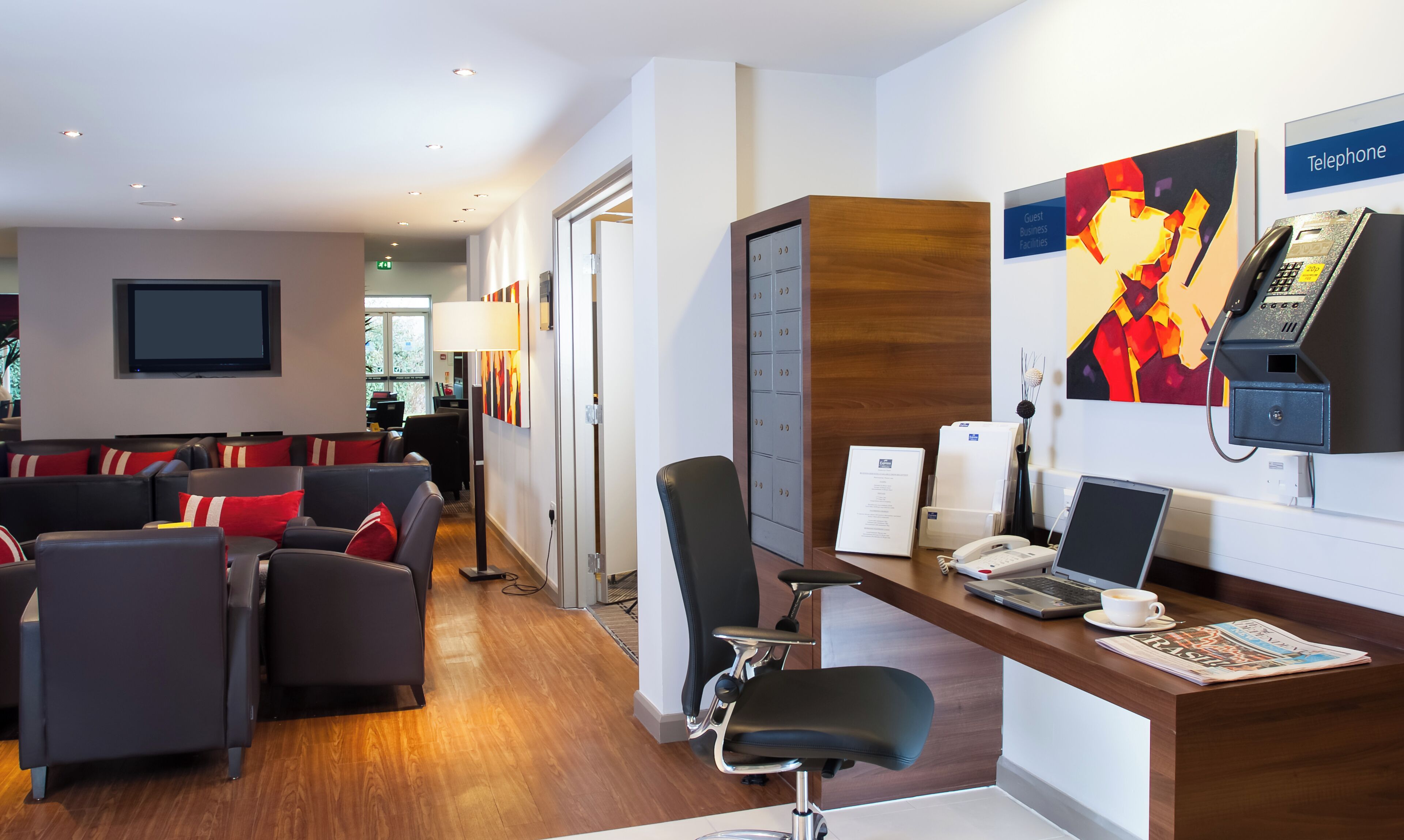 A hotel lobby with a reception desk, a seating area with sofas, a television, and a painting.